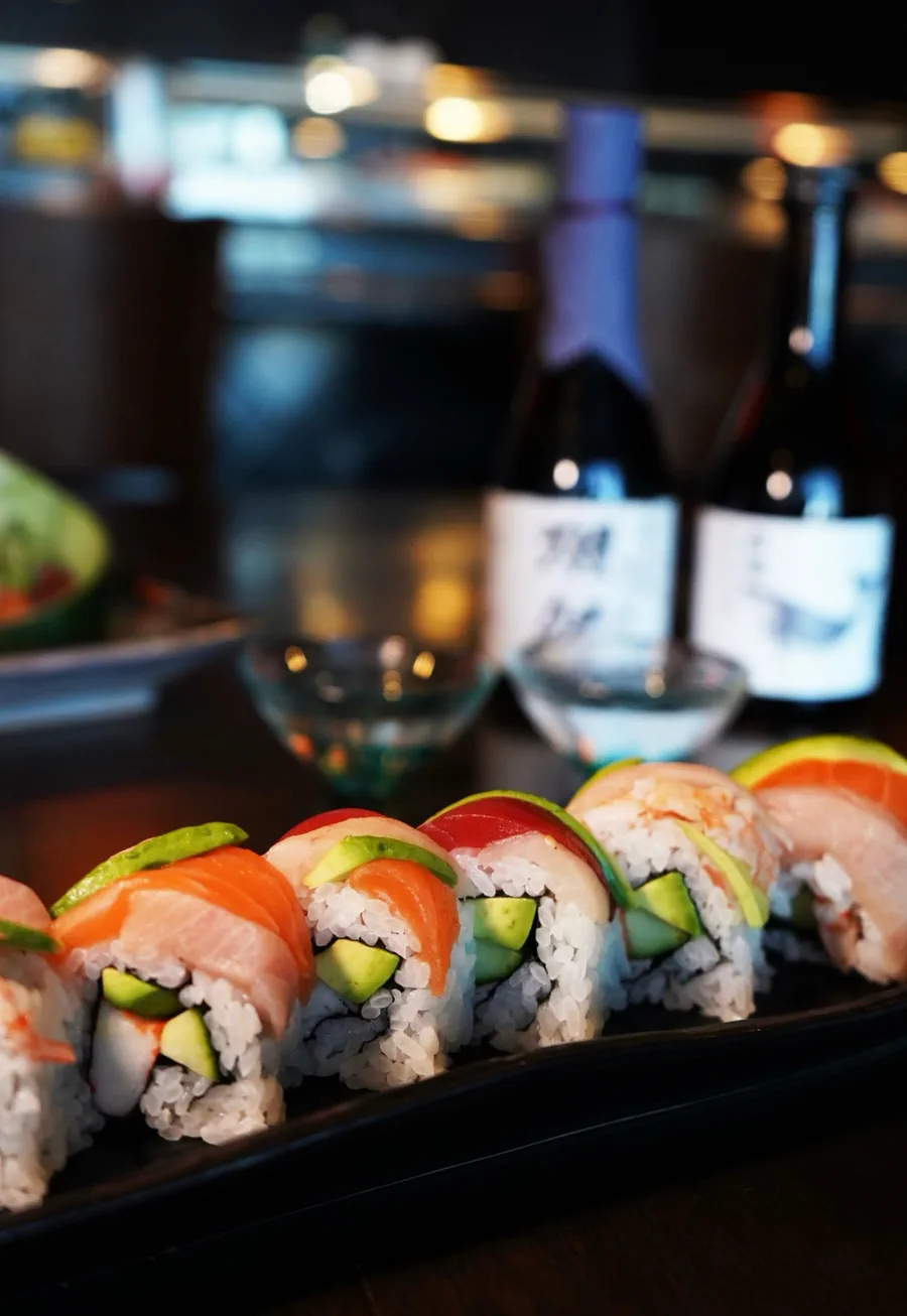 Rainbow roll topped with salmon, tuna, yellowtail, shrimp and avocado, with sake bottles behind