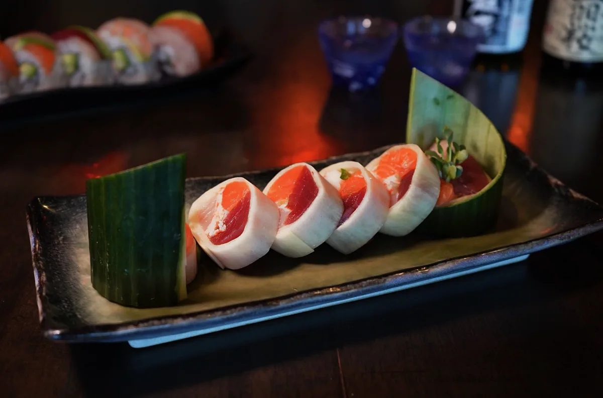 Sliced roll of salmon and tuna in a delicate white wrap, plated with cucumber and microgreens